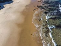 an aerial view of a beach and some rocks in the water and a person on the sand with a surfboard