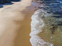 an aerial view of a beach and some rocks in the water and a person on the sand with a surfboard