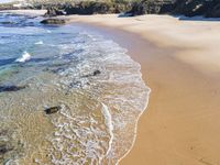 a white beach with two rocks and a sandy shore, and water running around the shore