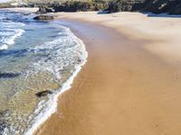 a white beach with two rocks and a sandy shore, and water running around the shore