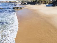 a white beach with two rocks and a sandy shore, and water running around the shore