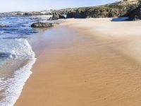 a white beach with two rocks and a sandy shore, and water running around the shore