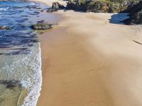 a sandy beach with some waves and the shore of the water covered by rocks and sand