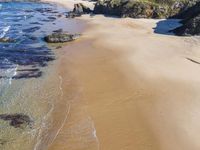 a sandy beach with some waves and the shore of the water covered by rocks and sand