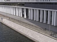 a man riding a bicycle by a waterway on the shore of a lake between two buildings