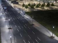 an empty roadway with lights on at night with cars passing by it and green grass