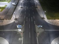 two roads in a empty intersection at night with a car going by and a person crossing it