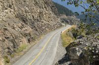 a motorcycle rider rides down a mountain road next to rocky cliffs and trees as seen from a distance