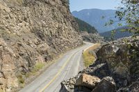 a motorcycle rider rides down a mountain road next to rocky cliffs and trees as seen from a distance