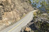 a motorcycle rider rides down a mountain road next to rocky cliffs and trees as seen from a distance