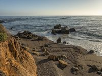 a grassy field by the shore and a cliff with rocks in the ocean in the background