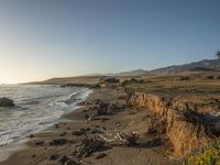 a grassy field by the shore and a cliff with rocks in the ocean in the background