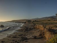 a grassy field by the shore and a cliff with rocks in the ocean in the background