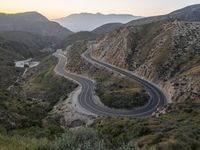 a curve highway in the hills with many lanes going through it at sunrise light and sun setting