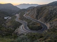 a curve highway in the hills with many lanes going through it at sunrise light and sun setting