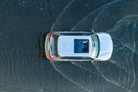 an overhead view of a car driving through the waves on a beach in front of a car