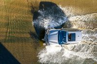 an aerial view of a car driving down some water on a road in the middle of the day