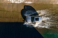 a car driving through the water in the ocean from above the side of a boat