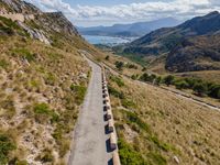 cars driving along a road in mountains area with mountains in the distance and blue sky