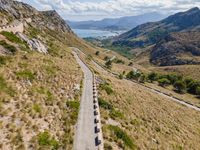 cars driving along a road in mountains area with mountains in the distance and blue sky