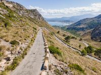 cars driving along a road in mountains area with mountains in the distance and blue sky