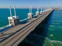 a bridge over the ocean with construction equipment in the background and two people walking on it