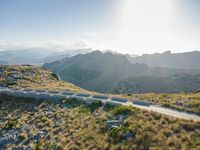 an aerial shot of the road between two mountains with water in the background and sunlight reflecting off of the mountains
