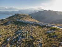 an aerial shot of the road between two mountains with water in the background and sunlight reflecting off of the mountains