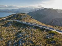 an aerial shot of the road between two mountains with water in the background and sunlight reflecting off of the mountains