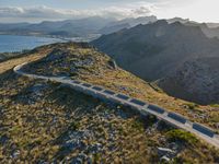 an aerial shot of the road between two mountains with water in the background and sunlight reflecting off of the mountains