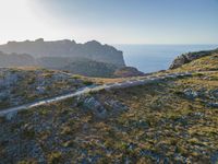 the dirt road runs along an rocky ridge beside the sea and cliffs with a mountain in the distance