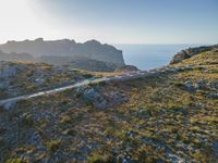 the dirt road runs along an rocky ridge beside the sea and cliffs with a mountain in the distance