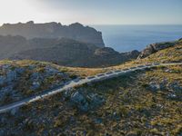 the dirt road runs along an rocky ridge beside the sea and cliffs with a mountain in the distance