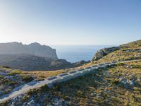 the dirt road runs along an rocky ridge beside the sea and cliffs with a mountain in the distance