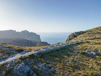 the dirt road runs along an rocky ridge beside the sea and cliffs with a mountain in the distance