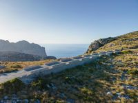 the dirt road runs along an rocky ridge beside the sea and cliffs with a mountain in the distance