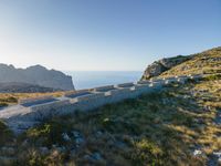 the dirt road runs along an rocky ridge beside the sea and cliffs with a mountain in the distance