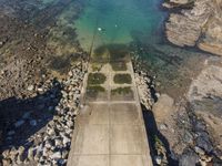 a rocky cliff overlooks a body of water and a dock with benches near it