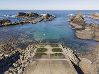 a rocky cliff overlooks a body of water and a dock with benches near it