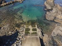 a rocky cliff overlooks a body of water and a dock with benches near it