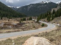 a mountain side with a road running next to the mountains, a bike parked in front of it and trees on one side