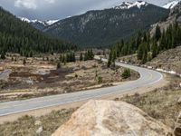 a mountain side with a road running next to the mountains, a bike parked in front of it and trees on one side