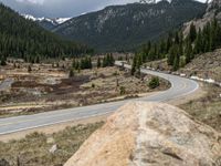 a mountain side with a road running next to the mountains, a bike parked in front of it and trees on one side