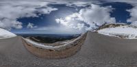 two roads with different angles and a view of mountains with clouds in the background and a street sign in the middle of each road