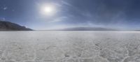 an aerial view of a frozen lake with mountains in the background and the sun beaming through the clouds