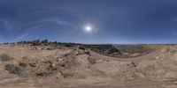 a fisheye lens image of a desert road and sun setting over a hill with sparse grass and bushes