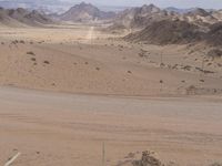 a person sitting on the beach next to a fence looking at an empty desert area