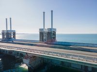 the road goes over an overpass into the ocean in front of an old power plant