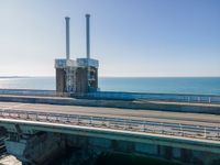 the road goes over an overpass into the ocean in front of an old power plant