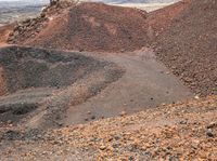 an open dirt field with two different rocks and gravel and a small hill in the background